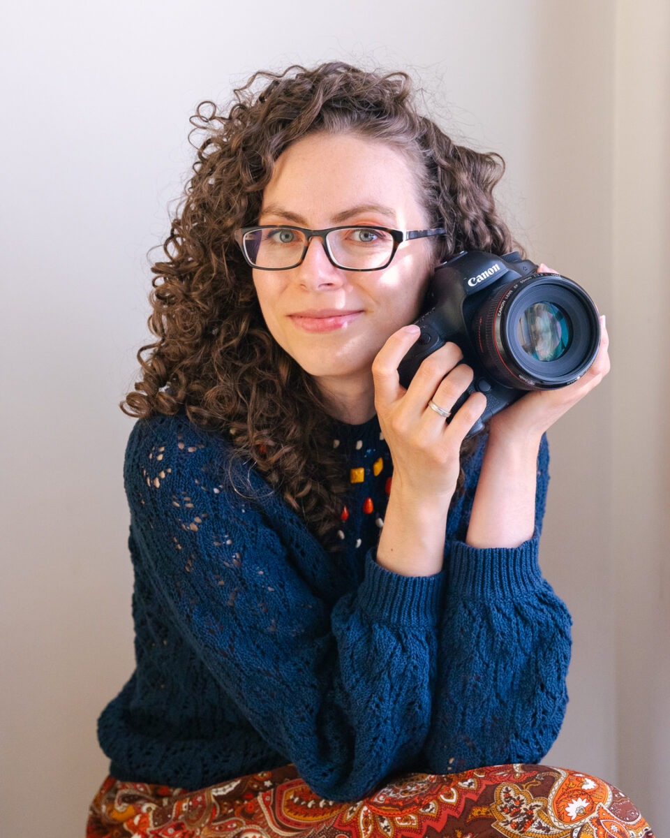 Ewa Kara, London photographer, sitting, holding camera and smiling